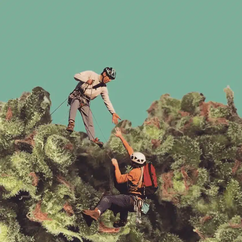 Two climbers in helmets and harnesses are on a rocky, moss-covered surface; one climber extends a hand to help the other up. The background is a plain teal color.