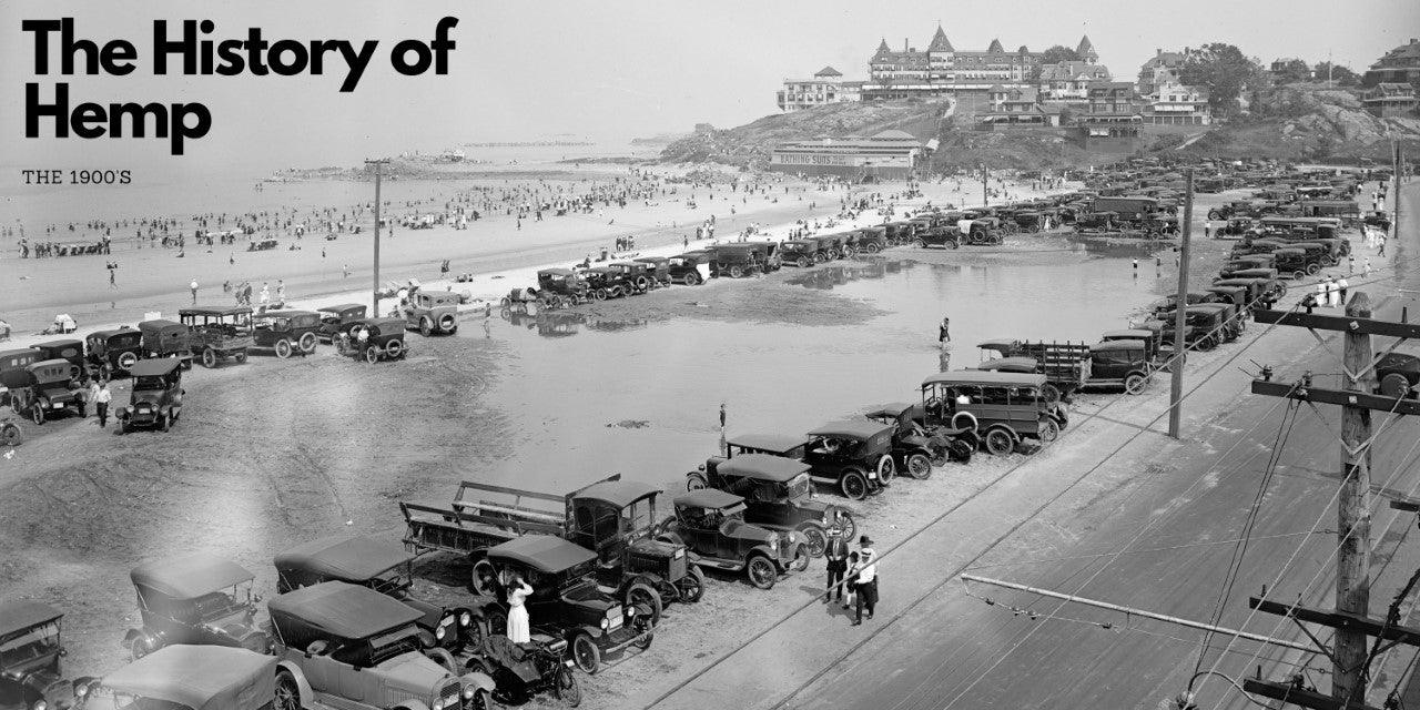 Black and white photo of 1900s cars parked by a busy beach, with crowds on the sand and buildings on a hill in the background. Text reads "The History of Hemp - The 1900s.