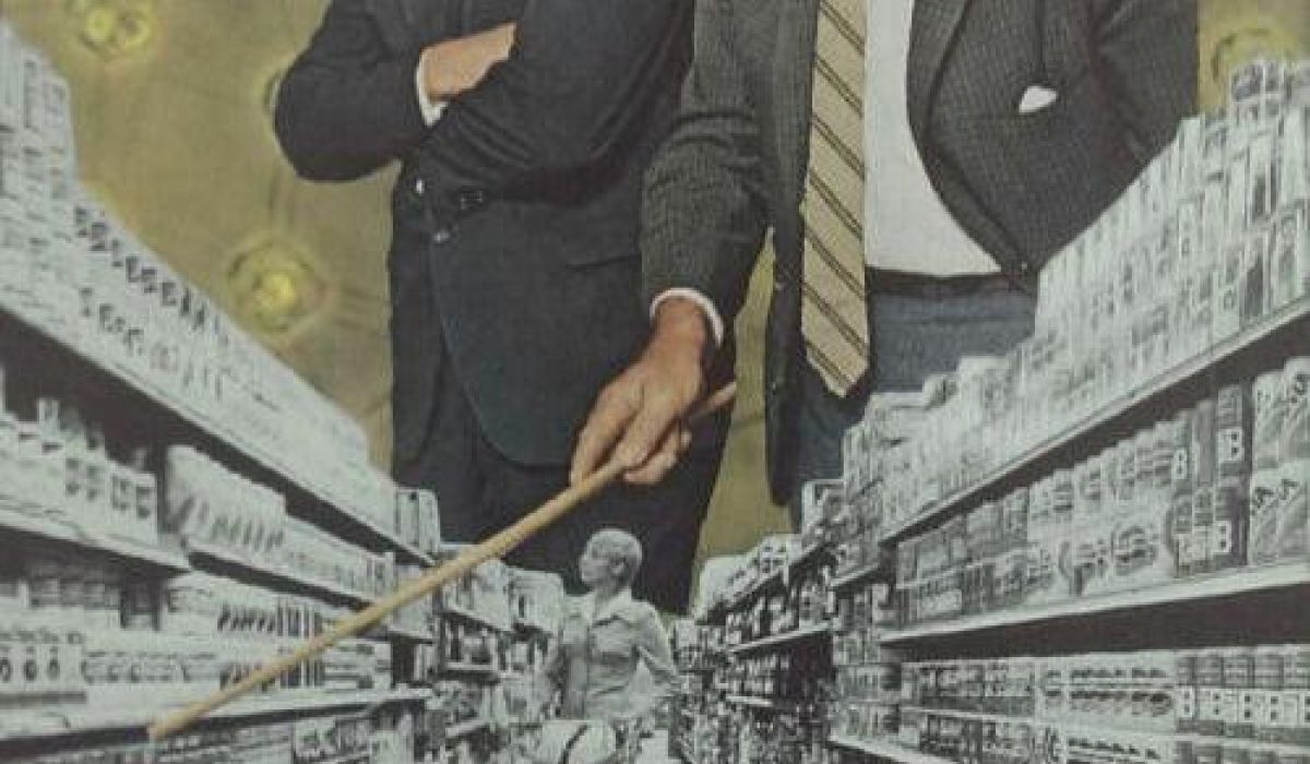 Two large men in suits stand above a supermarket aisle, with one pointing at shelves using a stick, while a woman shops below.